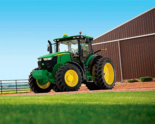 A full size John Deere tractor stands parked outside of a barn on a beautiful sunny day.